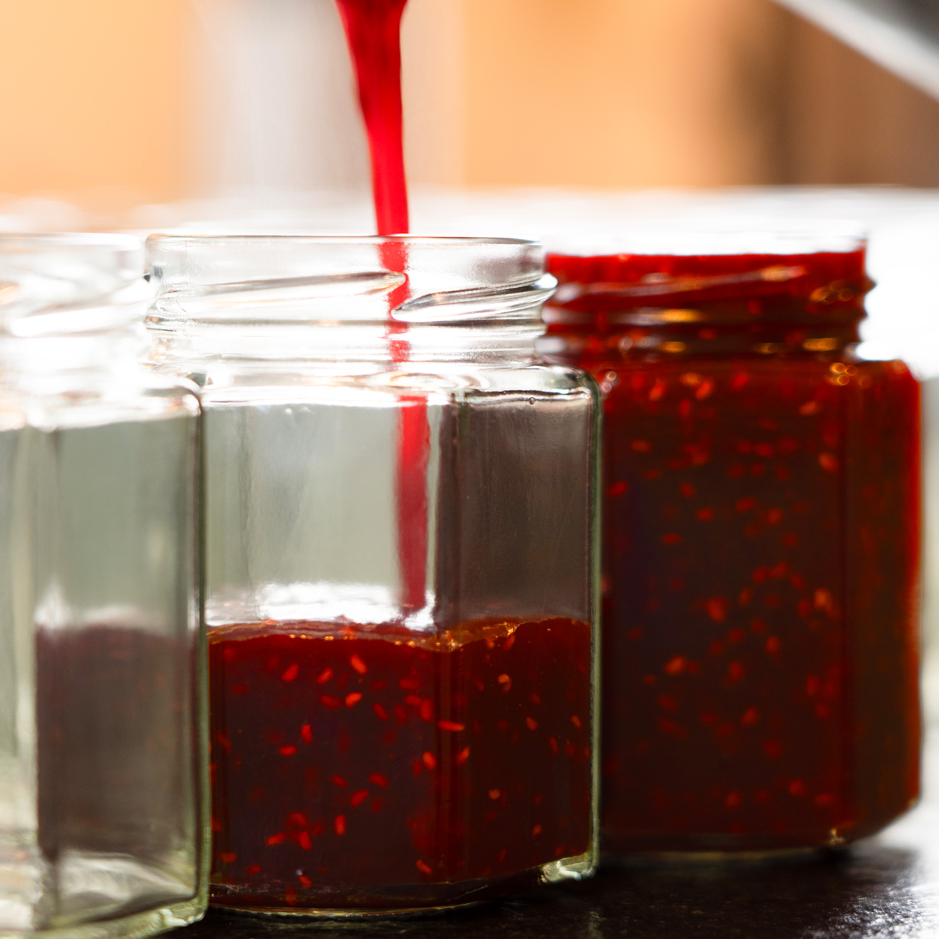 Mehrere Marmeladengläser werden in der Manufaktur mit frischer Konfitüre befüllt.