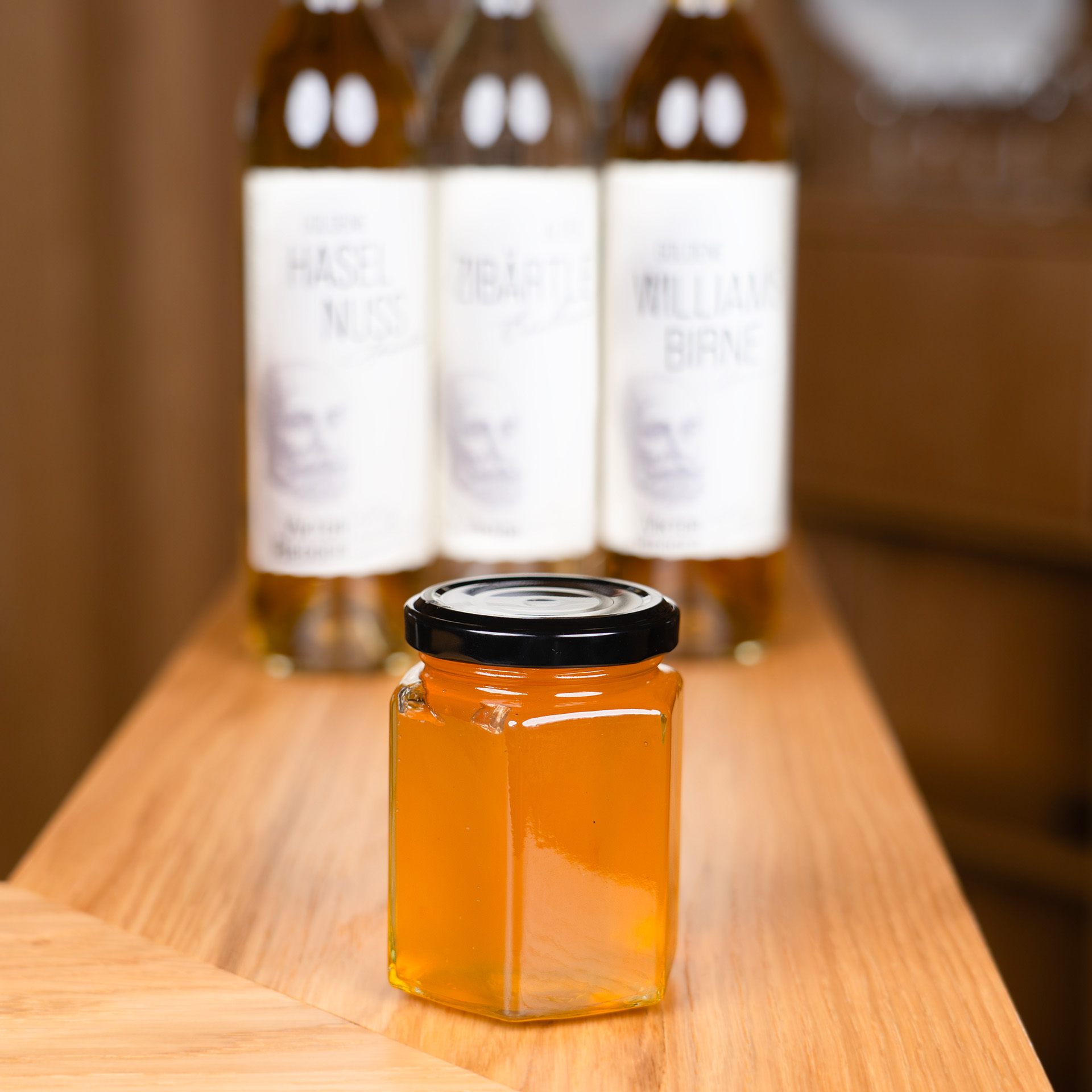 Marmeladenglas im Vordergrund, dahinter drei Flaschen mit Likören und Bränden – symbolisiert die natürliche Konservierung der Schwarzwälder Konfitüren.