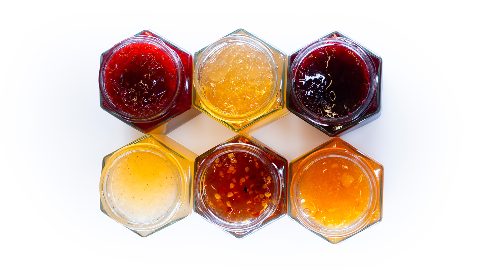 Sechs geöffnete Marmeladengläser aus der Vogelperspektive, gefüllt mit verschiedenen Schwarzwälder Konfitüren und Gelees.