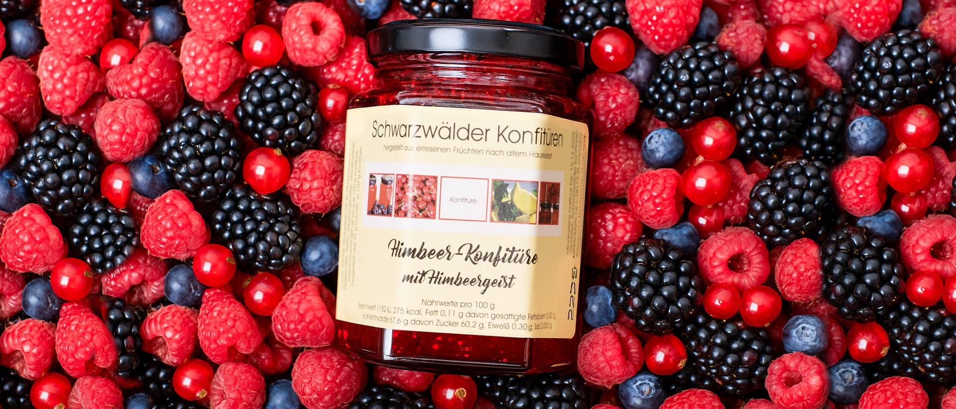 Ein Glas Schwarzwälder Konfitüre steht inmitten frischer, bunter Beeren – Symbol für natürliche Zutaten und handgemachten Genuss aus dem Schwarzwald.