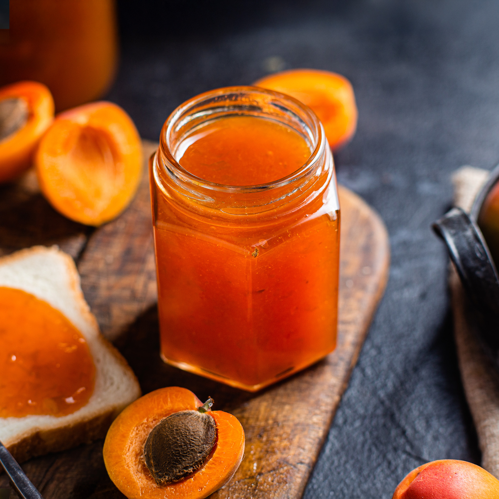 Orangenes Marmeladenglas auf einem Naturbrett, dekoriert mit Aprikosenstücken – Symbol für White-Label- und Private-Label-Konfitüren mit individuellem Etikett.