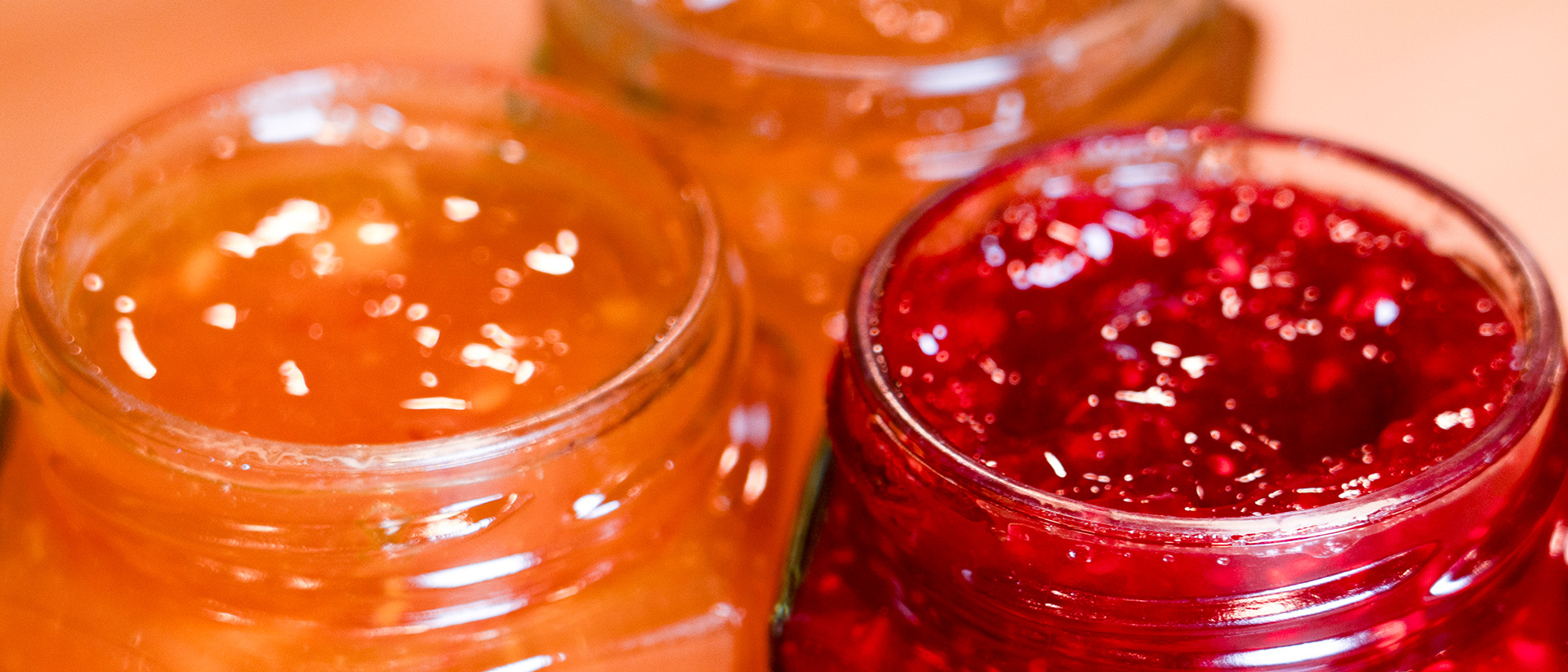 Drei Marmeladengläser ohne Deckel in Detailaufnahme, gefüllt mit frischer Konfitüre.